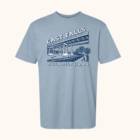 A light stone blue short-sleeve crewneck t-shirt featuring a vintage-style graphic of East Falls Twin Bridges with 'EAST FALLS' and 'PHILADELPHIA, PA' printed in white and dark blue.