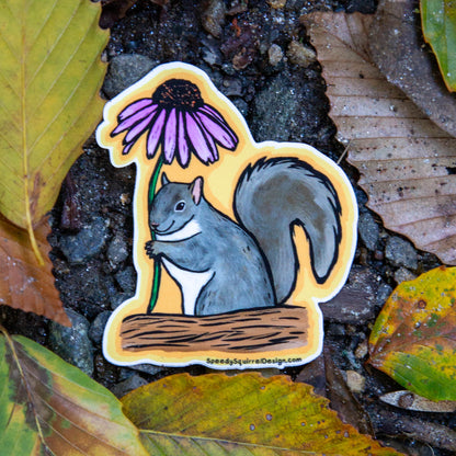 A die-cut sticker featuring a gray squirrel holding a purple coneflower, placed on wet forest leaves and soil. The sticker has a yellow border and the brand name SpeedySquirrelDesigns.com in the bototm left corner.