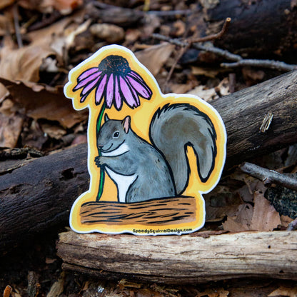 A die-cut sticker featuring a gray squirrel holding a purple coneflower on a yellow background, placed on a bed of dry leaves and branches outdoors.