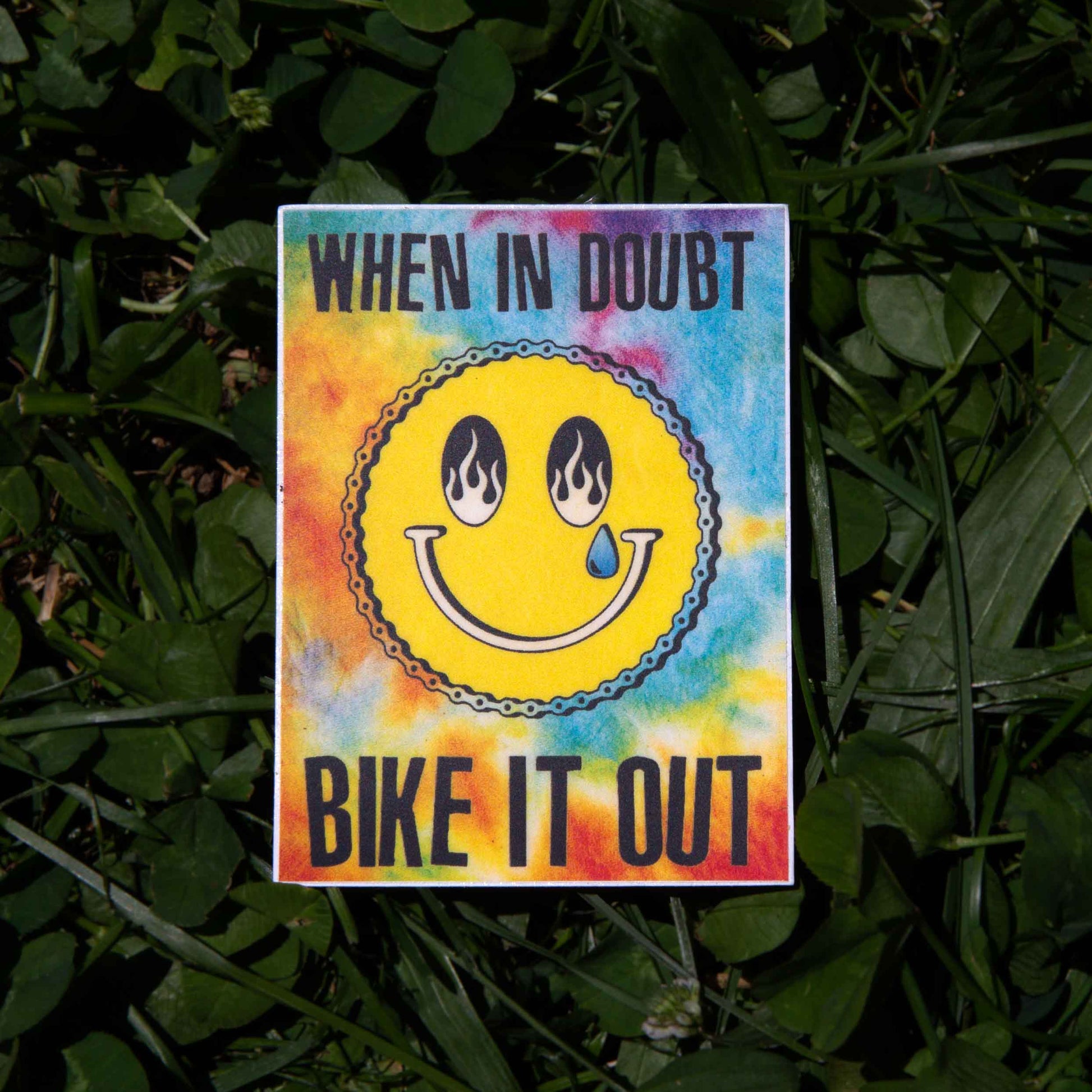Colorful sticker with a smiley face and text 'When in doubt, bike it out' on a grass background