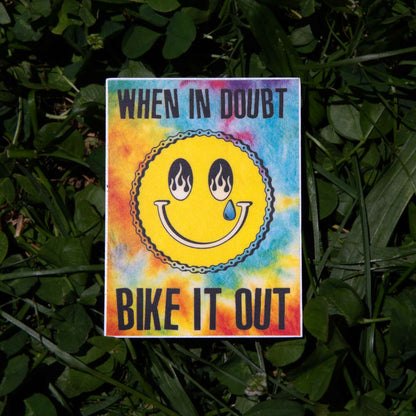 Colorful sticker with a smiley face and text 'When in doubt, bike it out' on a grass background
