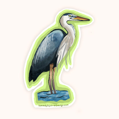 A die-cut sticker featuring a painted blue-gray heron standing in shallow blue water, with a white border and a bright green shadow effect behind it, shown on a plain light background. The website SpeedysSquirrelDesign.