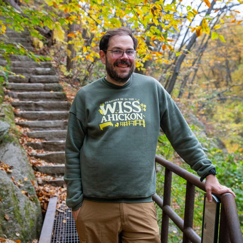 Man wearing a green sweatshirt with 'WISS Ahickon' text standing on stone steps in a forest.