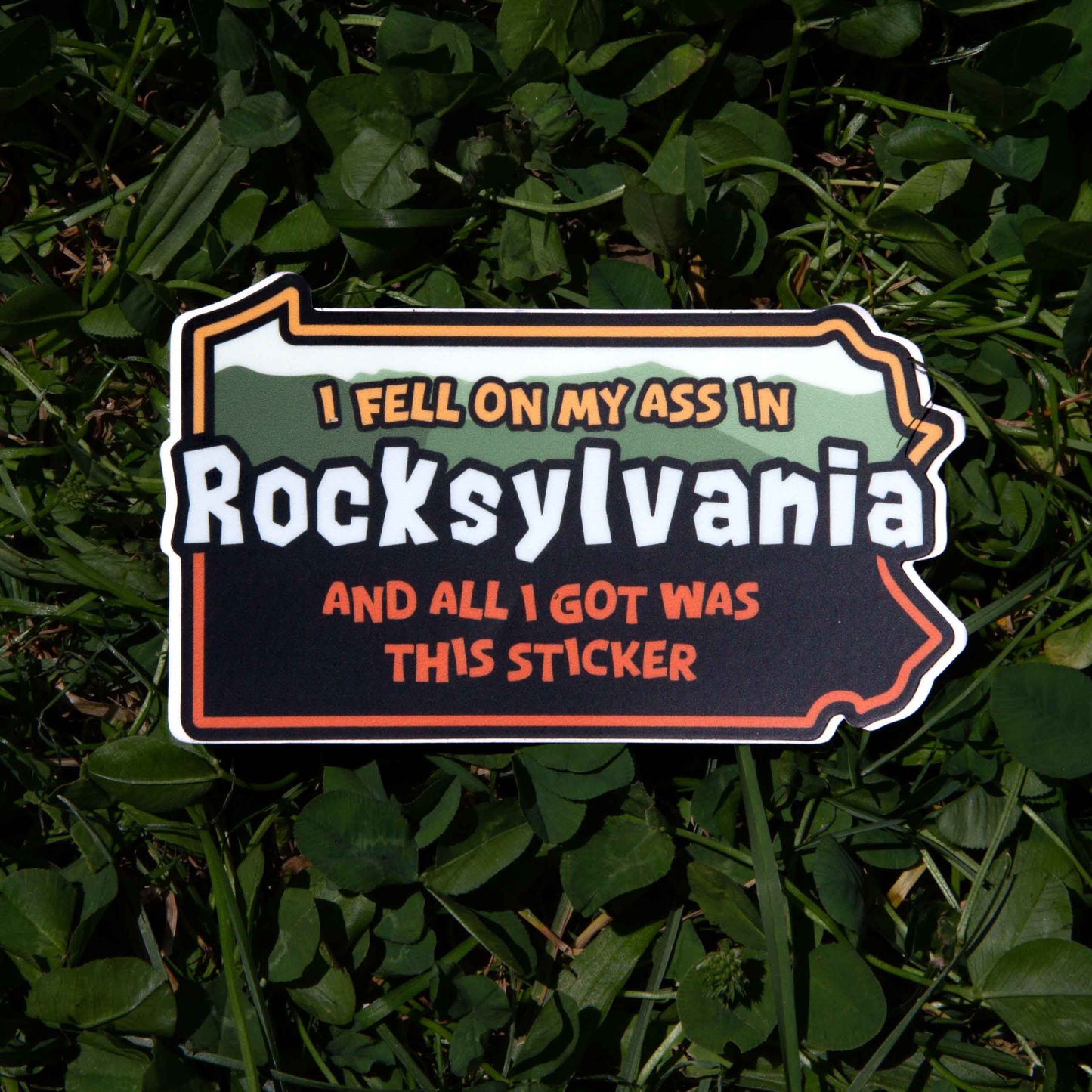Pennsylvania shaped sticker with text 'I fell on my ass in Rocksylvania and all I got was this sticker' on grass