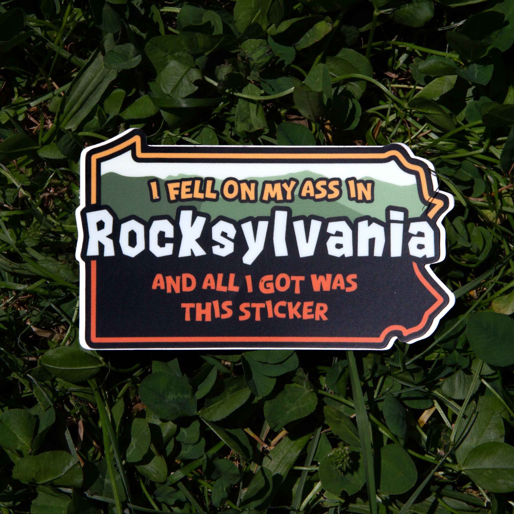 Pennsylvania shaped sticker with text 'I fell on my ass in Rocksylvania and all I got was this sticker' on grass