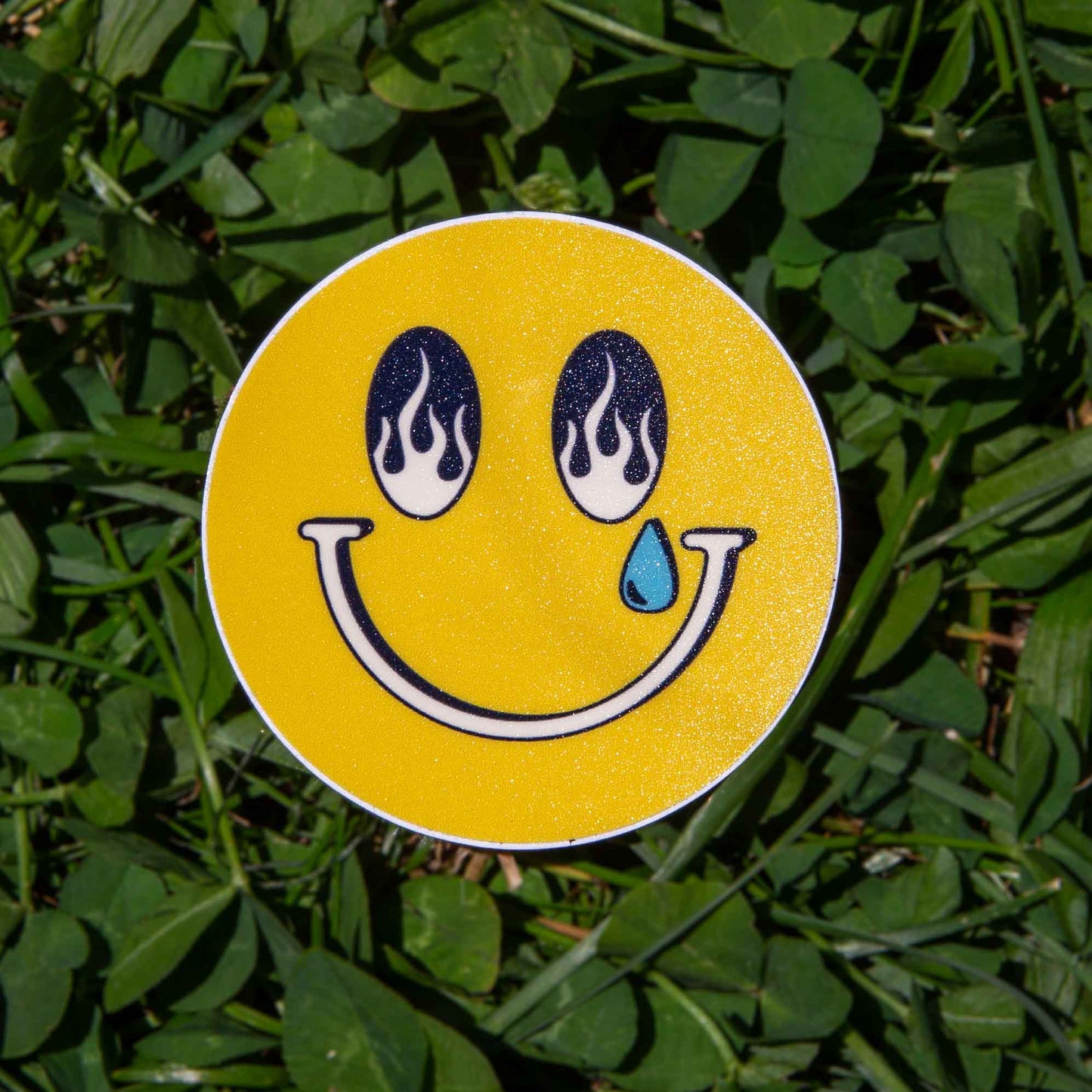 Smiley face sticker with flame eyes and a tear on grass