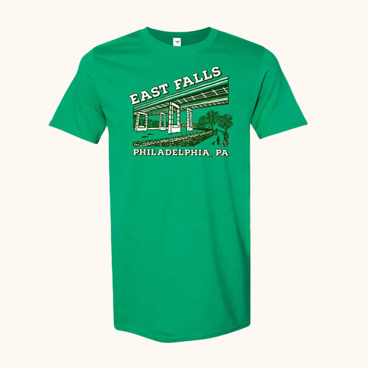 A green short-sleeve crewneck t-shirt featuring a vintage-style graphic of East Falls Twin Bridges with 'EAST FALLS' and 'PHILADELPHIA, PA' printed in white and dark green.