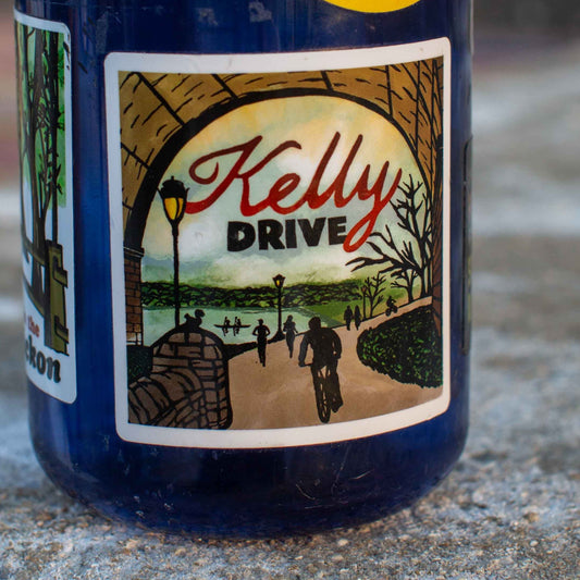 Bottle with a 'Kelly Drive' illustration sticker on a concrete surface. 