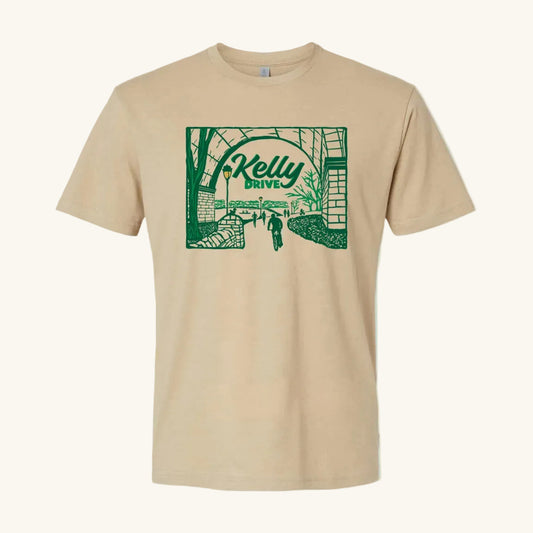 Beige t-shirt with 'Kelly Drive' design featuring a scenic view or bikers, runners and rowers on a trail, on a light blue background. 