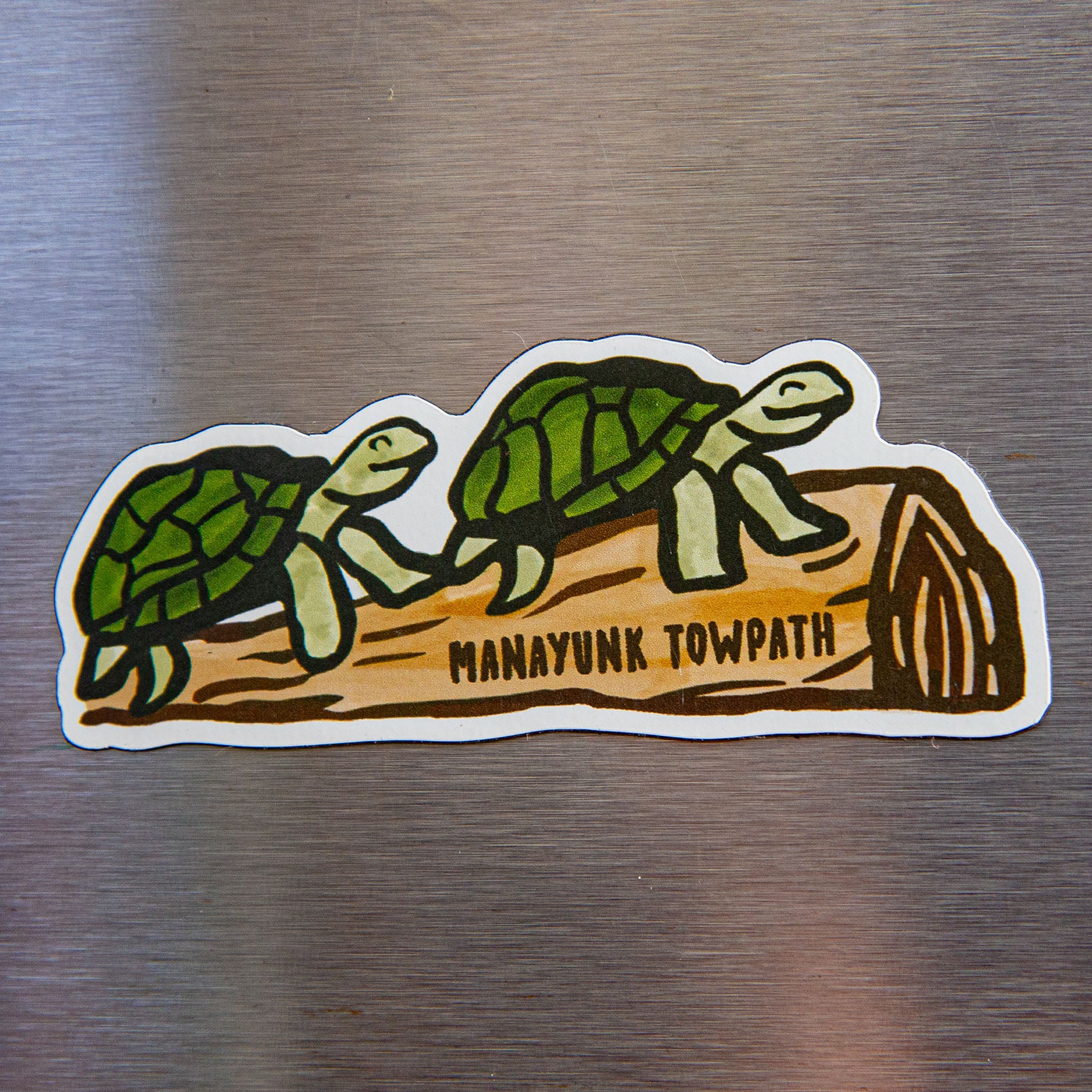  two turtles resting on a log with "Manayunk Towpath" written across it on a metallic background. 