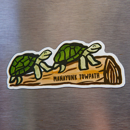  two turtles resting on a log with "Manayunk Towpath" written across it on a metallic background. 
