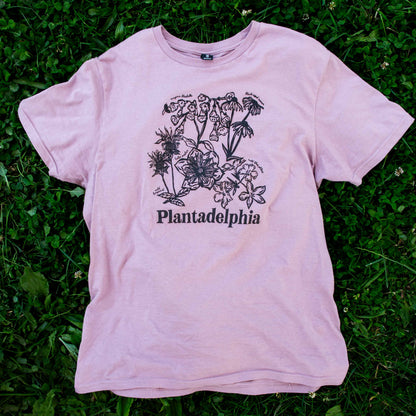 Lilac t-shirt with floral design and 'Plantadelphia' text on a grassy background
