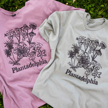 Two t-shirts with floral design and 'Plantadelphia' text on grass
