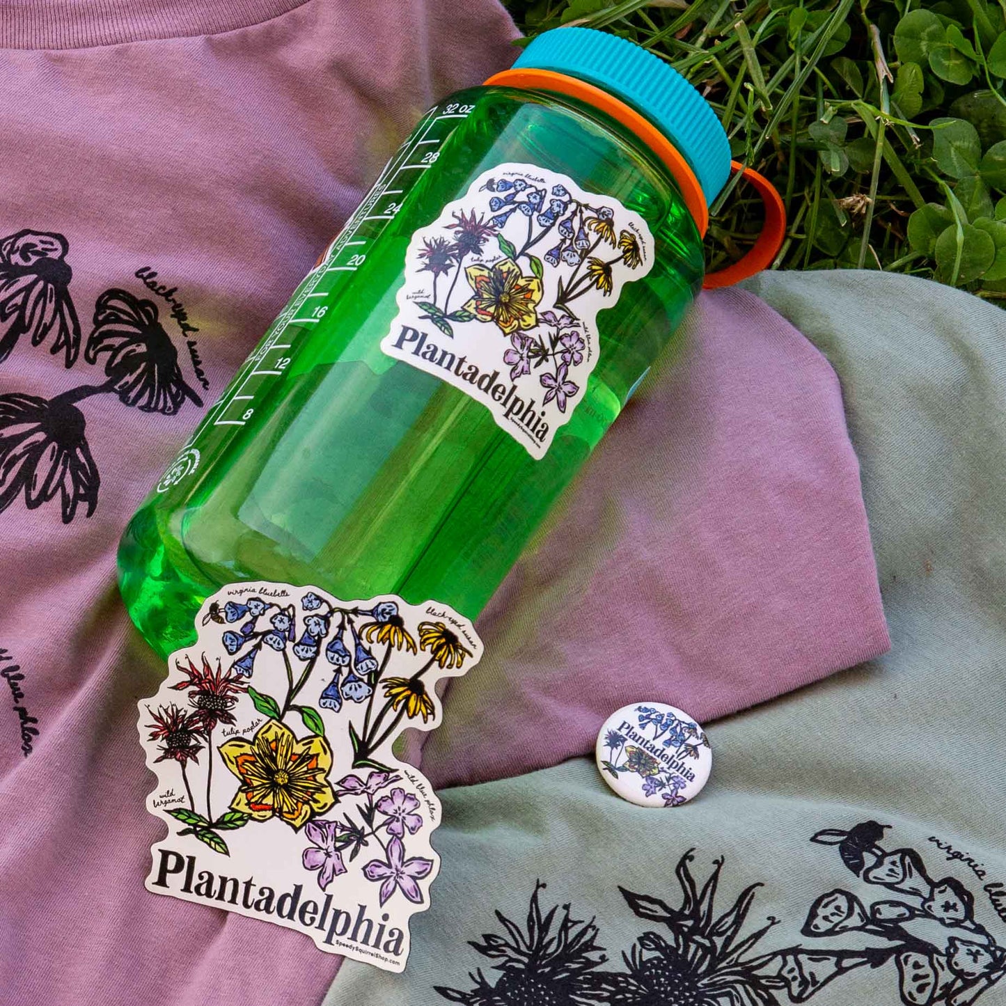Plantadelphia floral sticker design on a water bottle, the magnet and pin design are laying next to it.