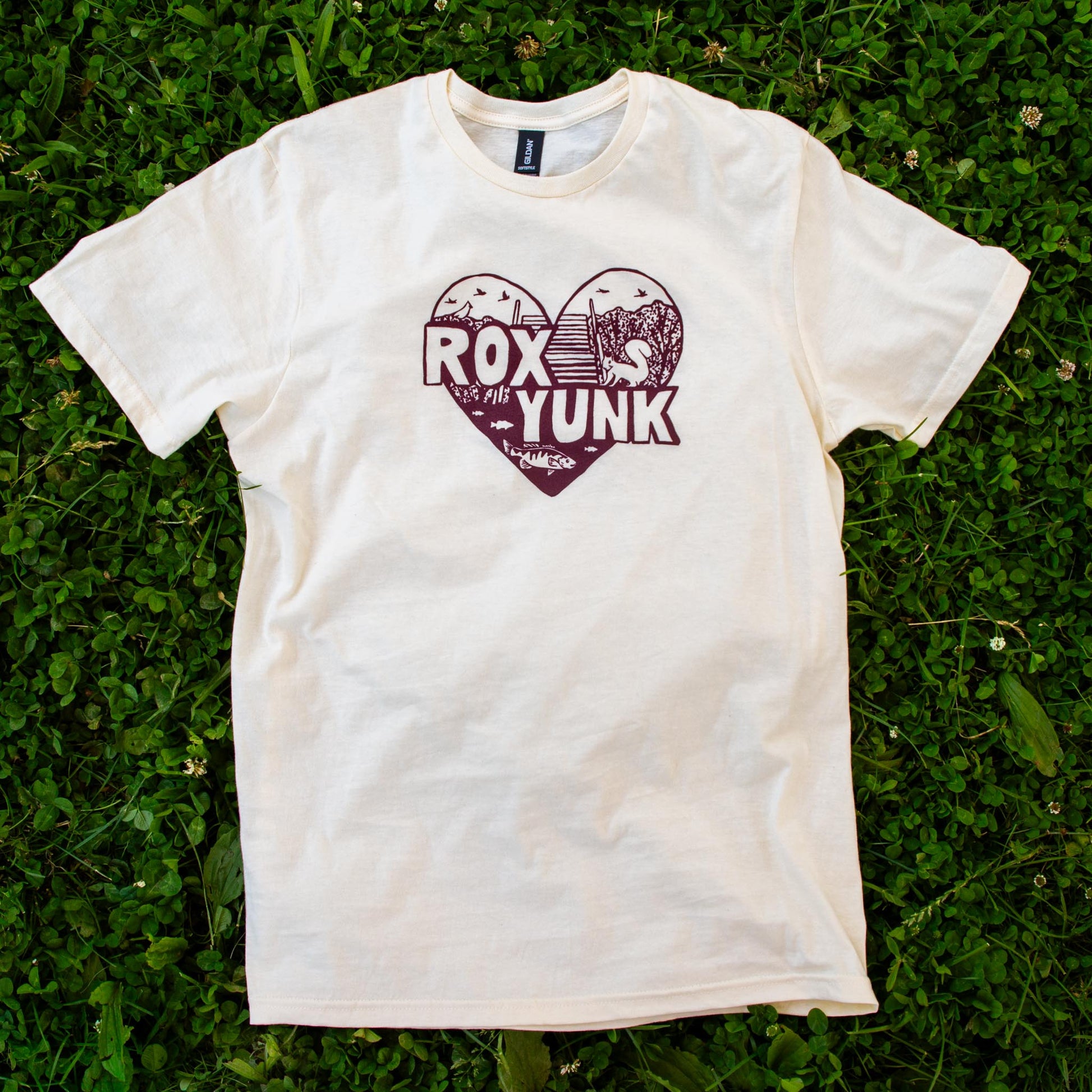 Cream t-shirt with 'RoxYunk' graphic laying on grass