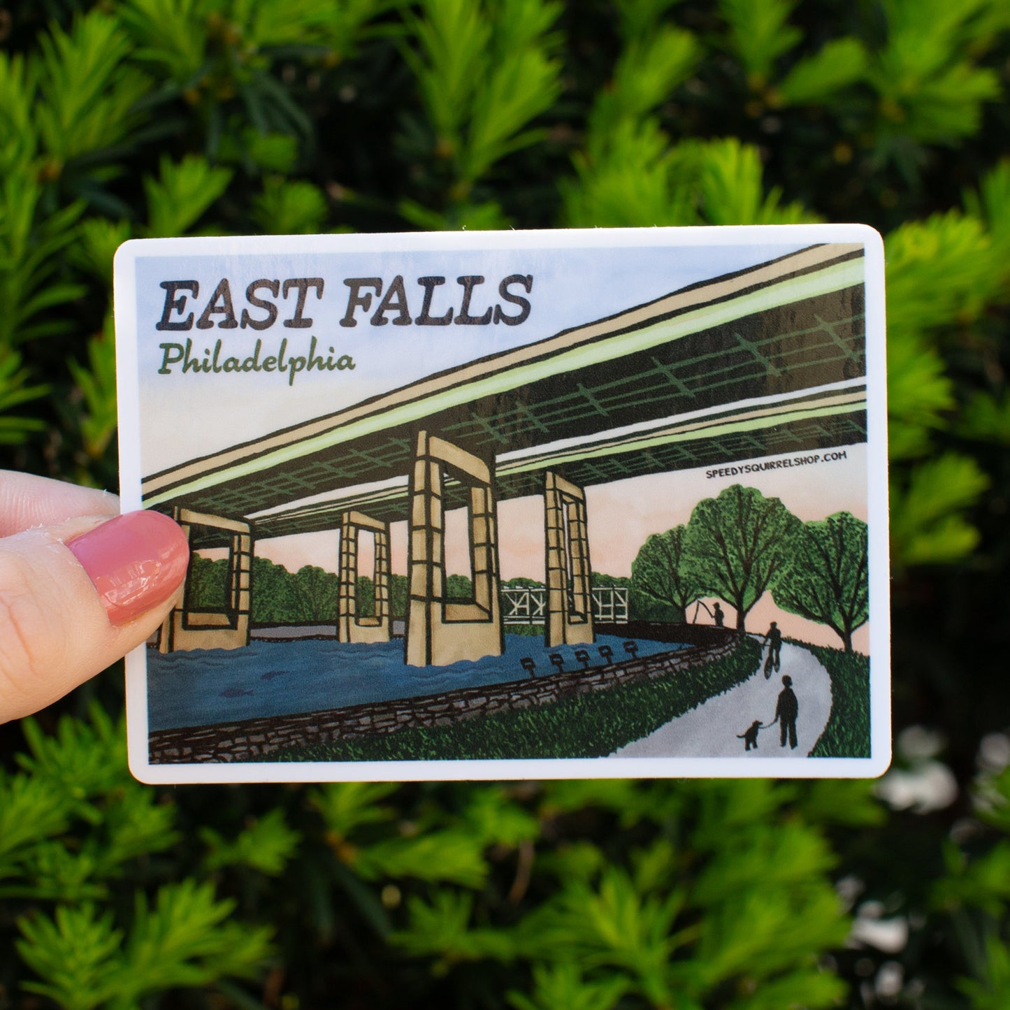Sticker of East Falls, Philadelphia held in front of green foliage