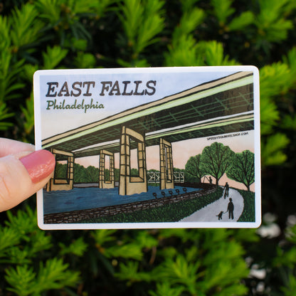 Sticker of East Falls, Philadelphia held in front of green foliage