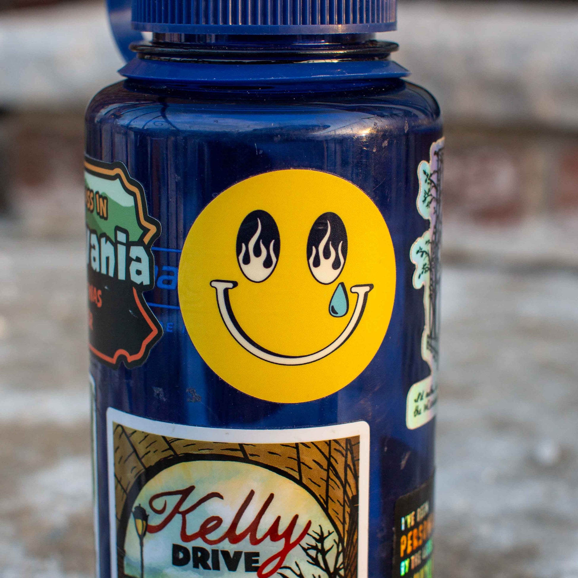 Blue bottle with stickers, including a smiley face sticker with flame eyes and a single tear.