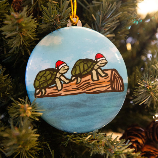 Two smiling turtle in santa hats relaxing on a floating login water on a circle Christmas ornament hanging on tree.