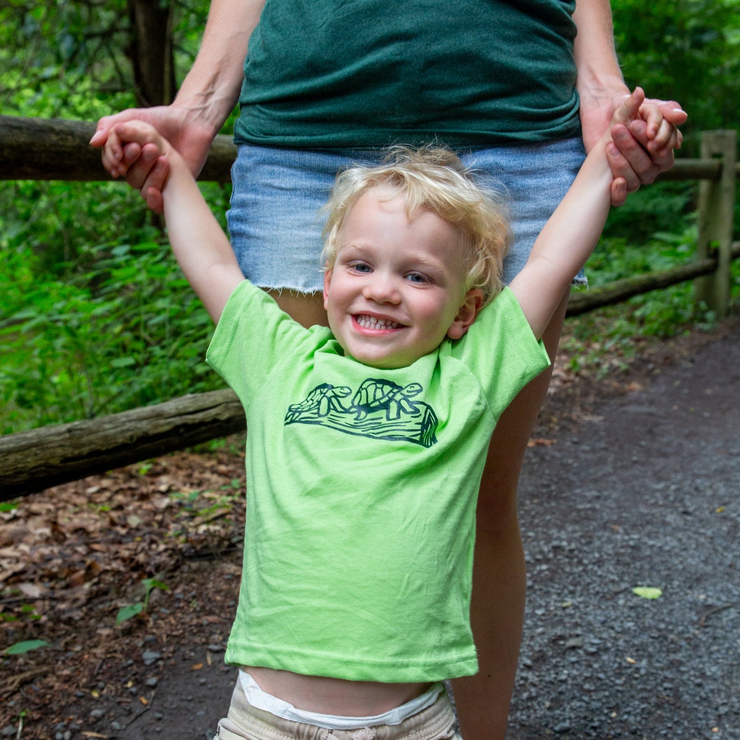 Child in a green shirt with turtle design held by an adult outdoors