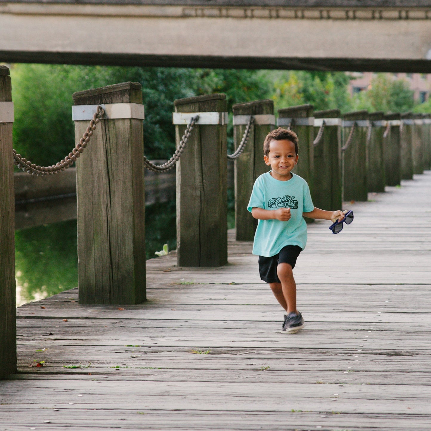Child running on a wooden dock with a bridge in the background