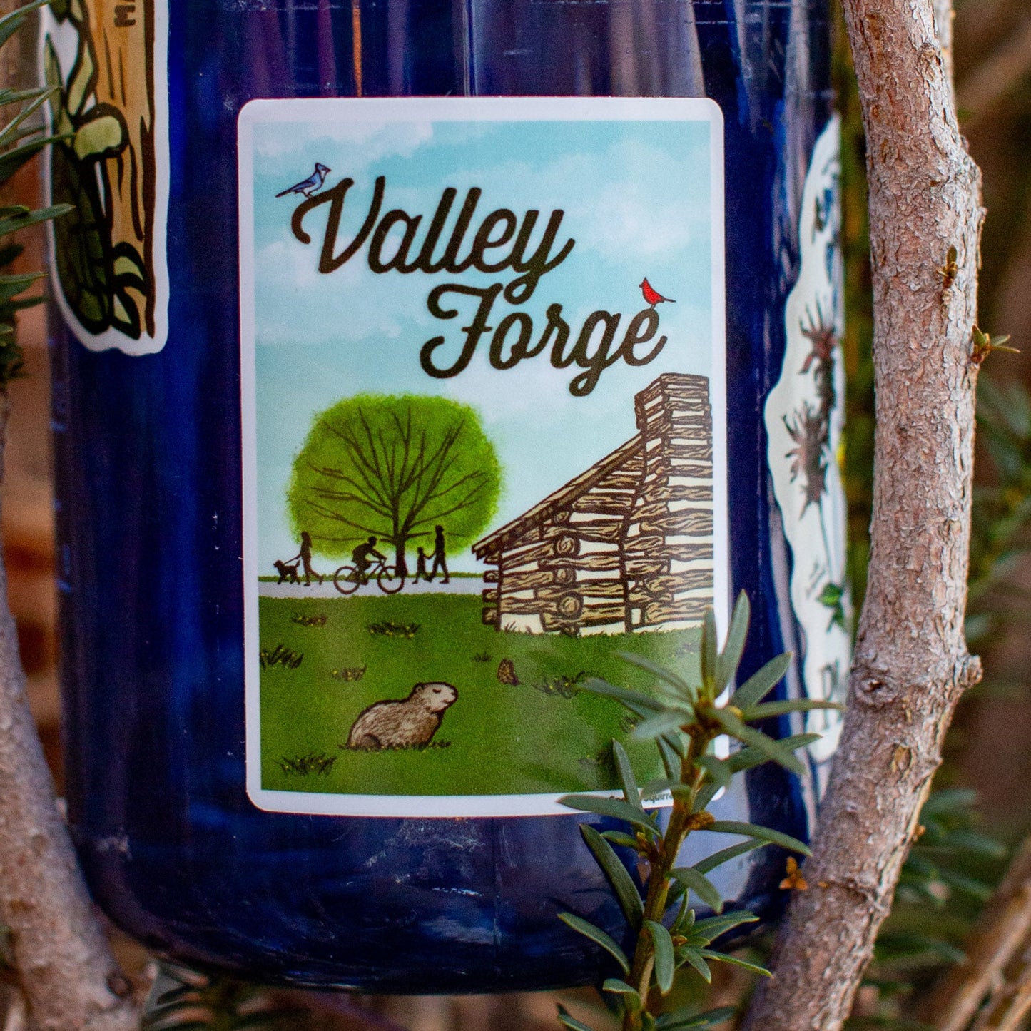Blue water bottle with a Valley Forge sticker Illustration of a log cabin, tree, and people on a bike and footpath.