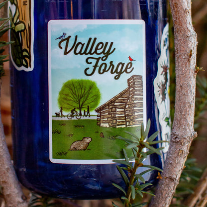 Blue water bottle with a Valley Forge sticker Illustration of a log cabin, tree, and people on a bike and footpath.
