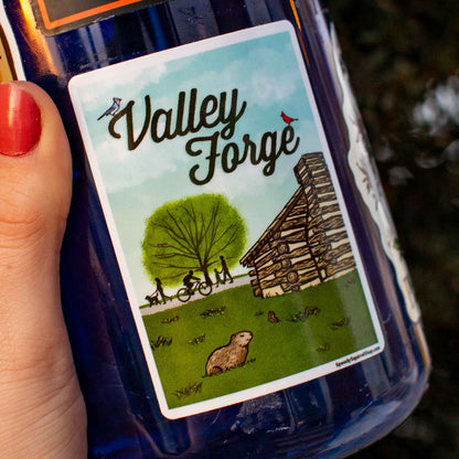 Bottle with a 'Valley Forge' sticker featuring illustrations of a cabin, tree, and people.