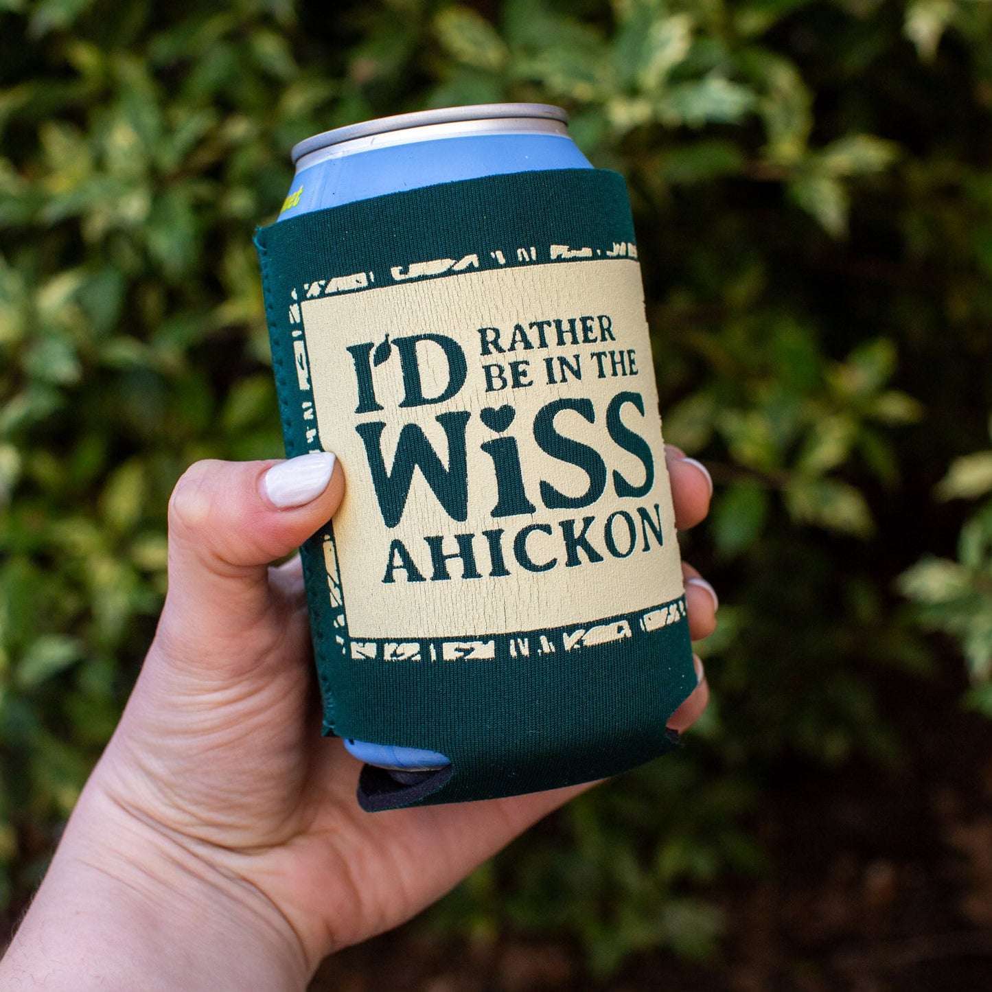 Hand holding a can with 'I'd Rather Be in the Wissahickon' text against a green leafy background