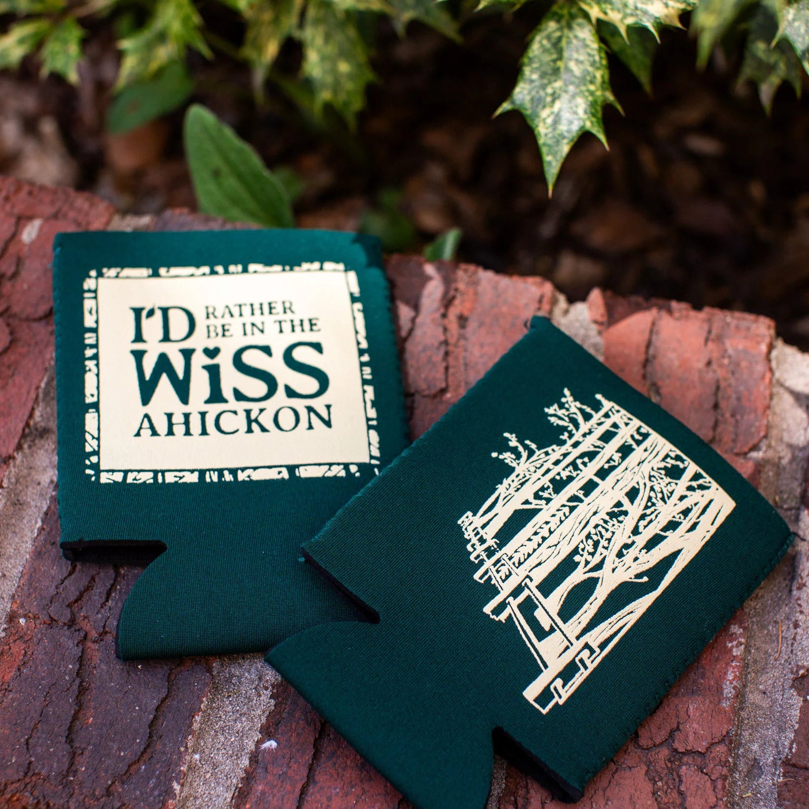 Two green can coolers with printed text on a brick surface.