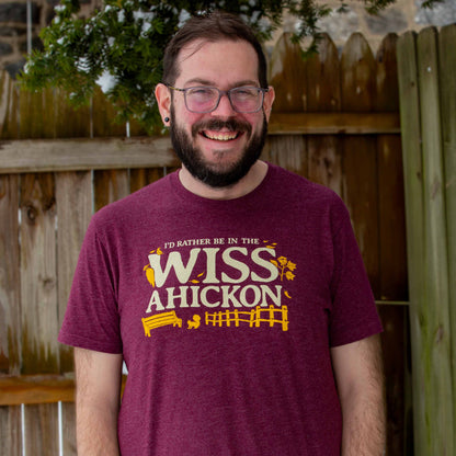 Man wearing a maroon t-shirt with 'I'd rather be in the Wissahickon' text and graphics outdoors.