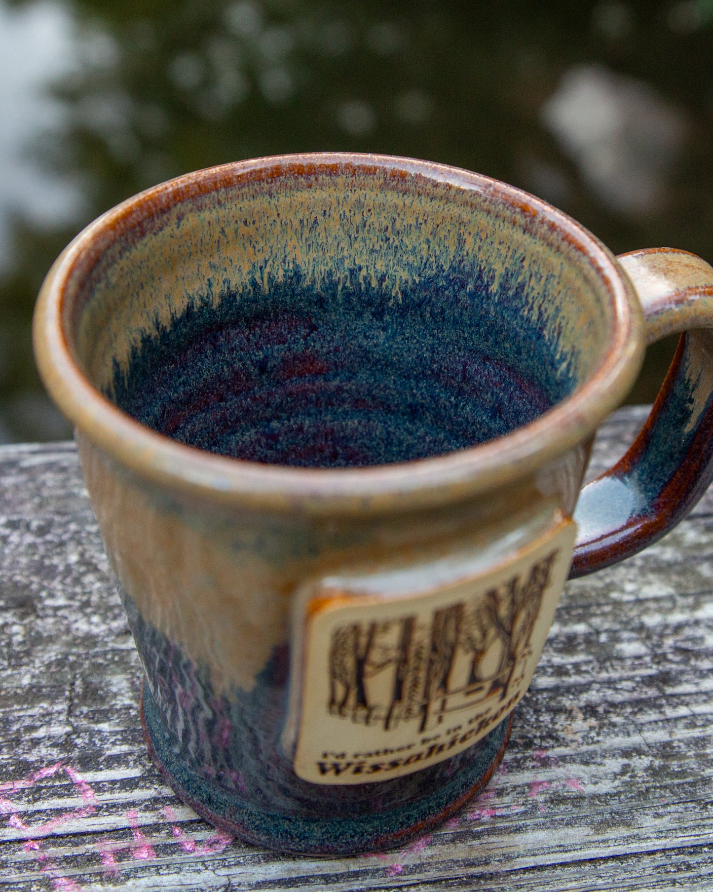 Handmade ceramic mug with blue interior and brown exterior on a wooden surface.