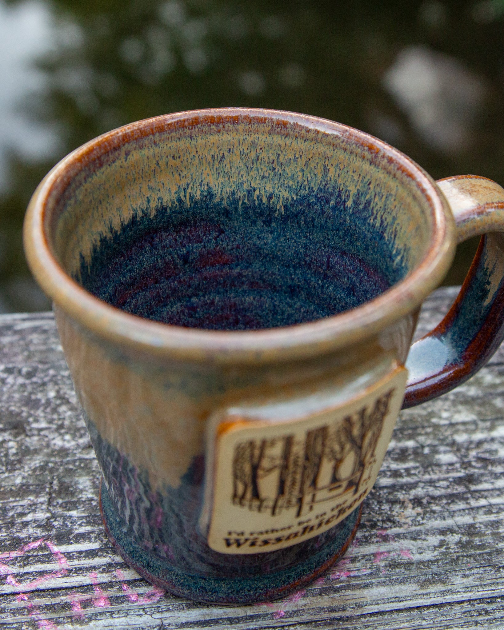 Handmade ceramic mug with blue interior and brown exterior on a wooden surface.