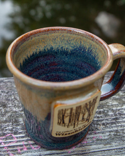 Handmade ceramic mug with blue interior and brown exterior on a wooden surface.