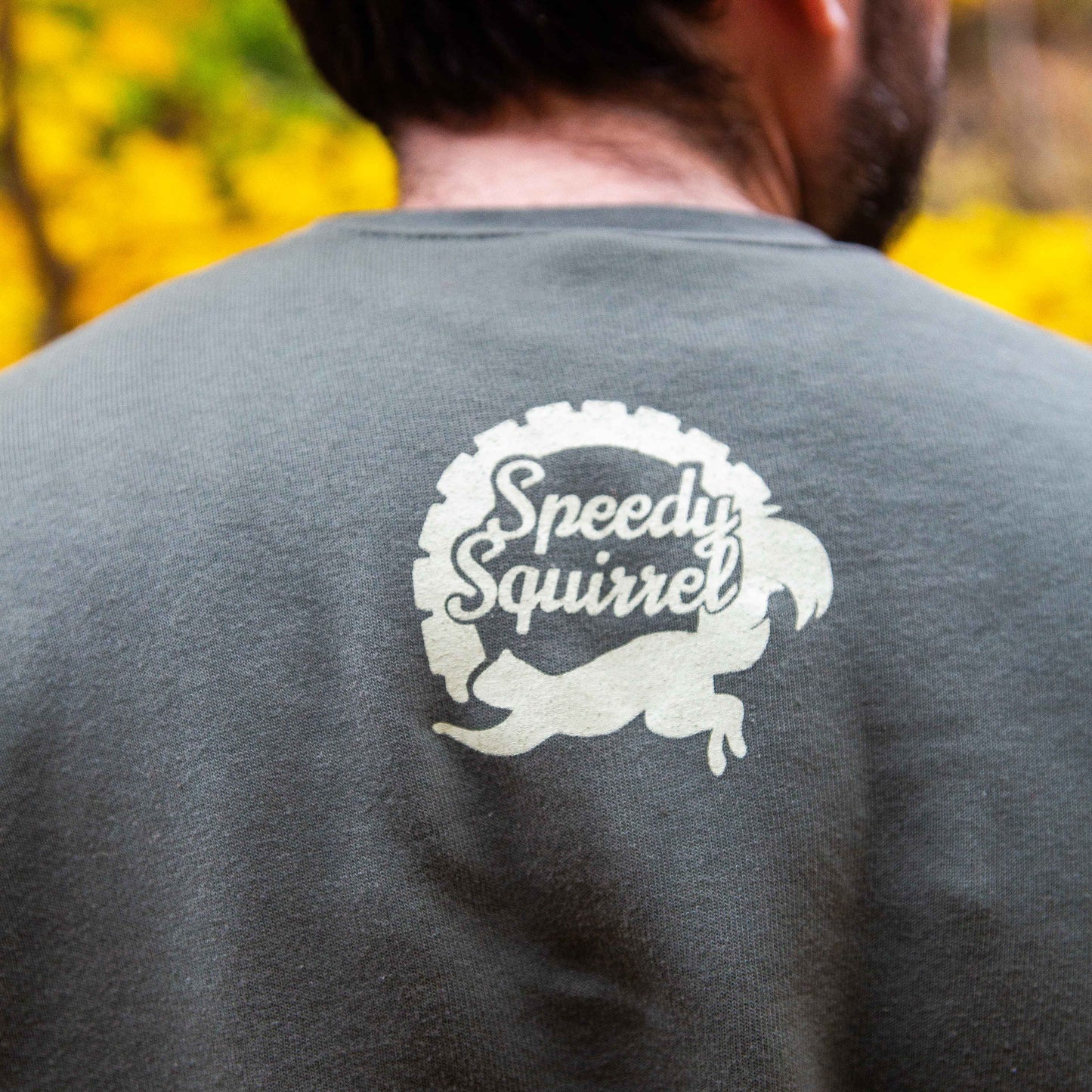Person wearing a gray shirt with 'Speedy Squirrel' logo, blurred natural background
